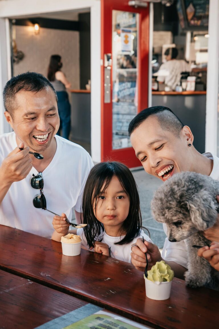 Cheerful LGBTQ+ family with their dog enjoying ice cream together outdoors.